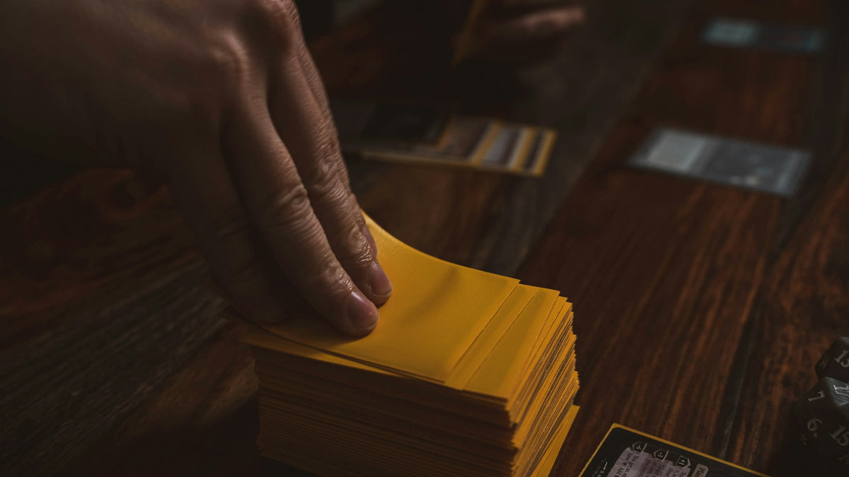 A hand drawing a card from a deck of matte card sleeves on a wooden game table